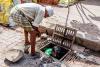 A person looking at a Christian sewage worker down a drain in Pakistan