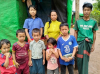 Christian family that have been displaced by violence standing infront of temporary plastic shelter in Myanmar