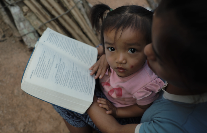 little girl looking at camera with lady reading the bible