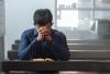 A man sitting on the Church pew praying with his Bible